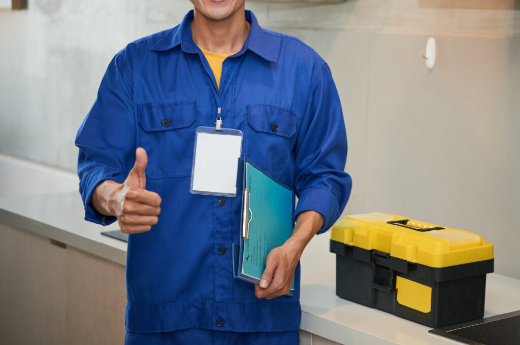 cheerful asian plumber standing near kitchen sink showing thumb up